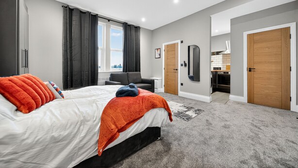 A modern bedroom with a large bed, a desk, and a view of the city. - Rosemont Road (Leeds)