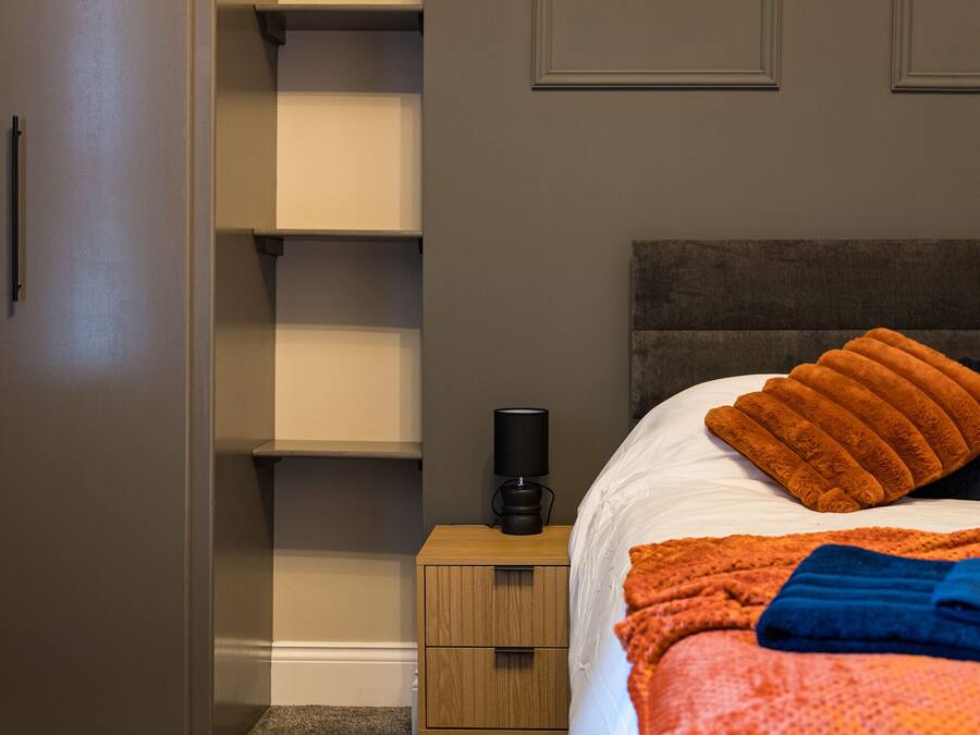 A bedroom with a bed, a nightstand, a lamp, and a wardrobe.