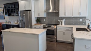 A modern kitchen with white cabinetry, stainless steel appliances, a central island, and a brick backsplash. - Queen City Castle - Spacious 3-bedroom townhome w Rooftop Terrace & City Views (Charlotte)