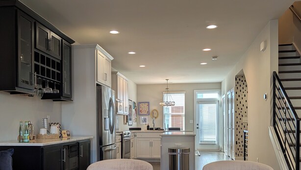 A modern living room with a round coffee table, two armchairs, and a sofa. A kitchen with white cabinets and a dining area is visible in the background. - Queen City Castle - Spacious 3-bedroom townhome w Rooftop Terrace & City Views (Charlotte)