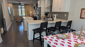 A modern kitchen with white cabinets, a central island, and black chairs. - Queen City Castle - Spacious 3-bedroom townhome w Rooftop Terrace & City Views (Charlotte)