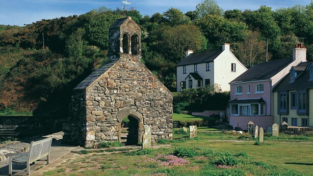 A stone church with a bell tower, surrounded by a grassy area with flowers and a bench. - Tan Y Bryn Y Beudy, Newport (Dinas Cross)
