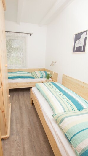 Une chambre avec deux lits en bois, une fenêtre donnant sur un beau paysage et un tableau encadré au mur.