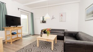 Ein modernes Wohnzimmer mit einer schwarzen Ledersofa, einem Holztisch, einem Fernseher auf einem Schrank und einem gemusterten Teppich.