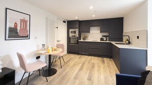 Una cocina moderna con armarios oscuros, un microondas, un horno y un lavabo. Hay una zona de comedor con una mesa redonda y dos sillas.