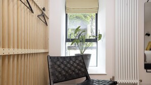Una habitación con un banco de cuero negro, una ventana con vistas a zonas verdes, un radiador y una pared de listones de madera.