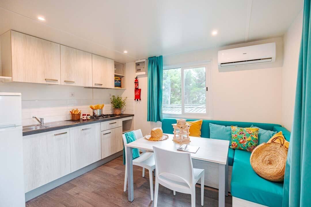 Une cuisine moderne avec des meubles blancs, une table à manger avec des chaises et un canapé de couleur turquoise agrémenté de coussins.