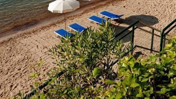 A beach with clear blue water, a sandy shore, and a hill in the background. There are two white umbrellas and two blue lounge chairs. - Camping Village Rosselba Le Palme Mobilehome Comfort for 4 persons (Portoferraio)