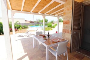 Un patio al aire libre con una mesa y sillas de madera, una piscina al fondo y un muro de piedra.