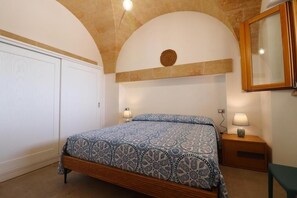 Un dormitorio con cama, dos lámparas de noche, mesita de noche, espejo y techo abovedado.
