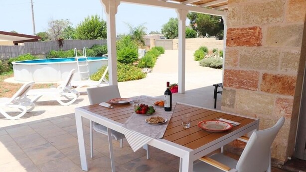 Eine Terrass mit Tisch für zwei Personen, ein Pool im Hintergrund und eine Steinmauer.