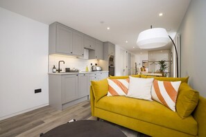 Ein modernes Wohnzimmer mit gelber Couch, Küchenbereich und Esstisch.