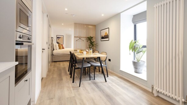 A modern kitchen with built-in appliances, a dining area with a table and chairs, and a large window with a view. - Argyl | Abbey Gate: Studio 4 (Edinburgh)