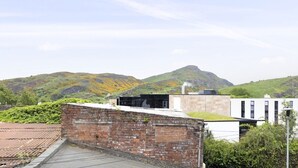 A building with a brick wall, a flat roof, and a view of green hills in the background. - Argyl | Abbey Gate: Studio 4 (Edinburgh)