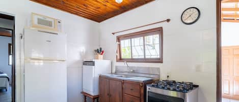 A compact kitchen with a wooden ceiling, a built-in microwave, a sink, a stove, and a clock on the wall.