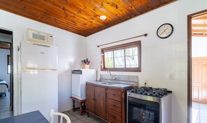 Cocina compacta con techo de madera, microondas integrado, fregadero, estufa y un reloj en la pared.