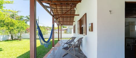 A covered outdoor area with a hammock, two lounge chairs, and a tiled patio.