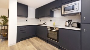 A modern kitchen with dark cabinets, a microwave, an oven, and a sink. - Argyl | Abbey Gate: Studio 3 (Edinburgh)