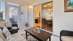 A covered patio with wicker furniture, a table with decorative items, and a sliding glass door leading to an interior dining area. - 3/2 Beautiful Home in Summerhill (The Villages)