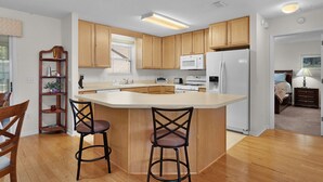 A modern kitchen with wooden cabinets, a central island with bar stools, a microwave, and a refrigerator. - 3/2 Beautiful Home in Summerhill (The Villages)