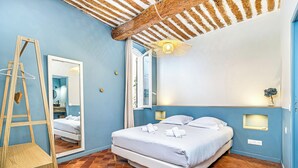 Un dormitorio con cama, espejo, lámpara colgante y ventana.