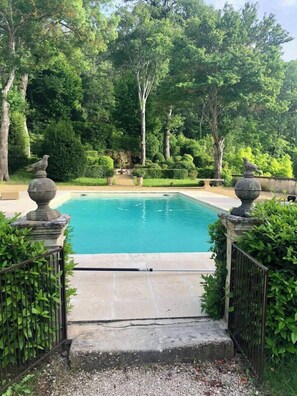 Ein rechteckiger Pool mit Steinbalustraden, umgeben von üppiger Vegetation und Bäumen.