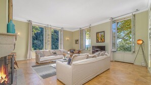 Un salón espacioso con chimenea, asientos cómodos, ventanas amplias y vistas al exterior.