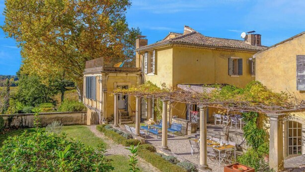 Un edificio amarillo con terraza, mesas al aire libre y jardín.