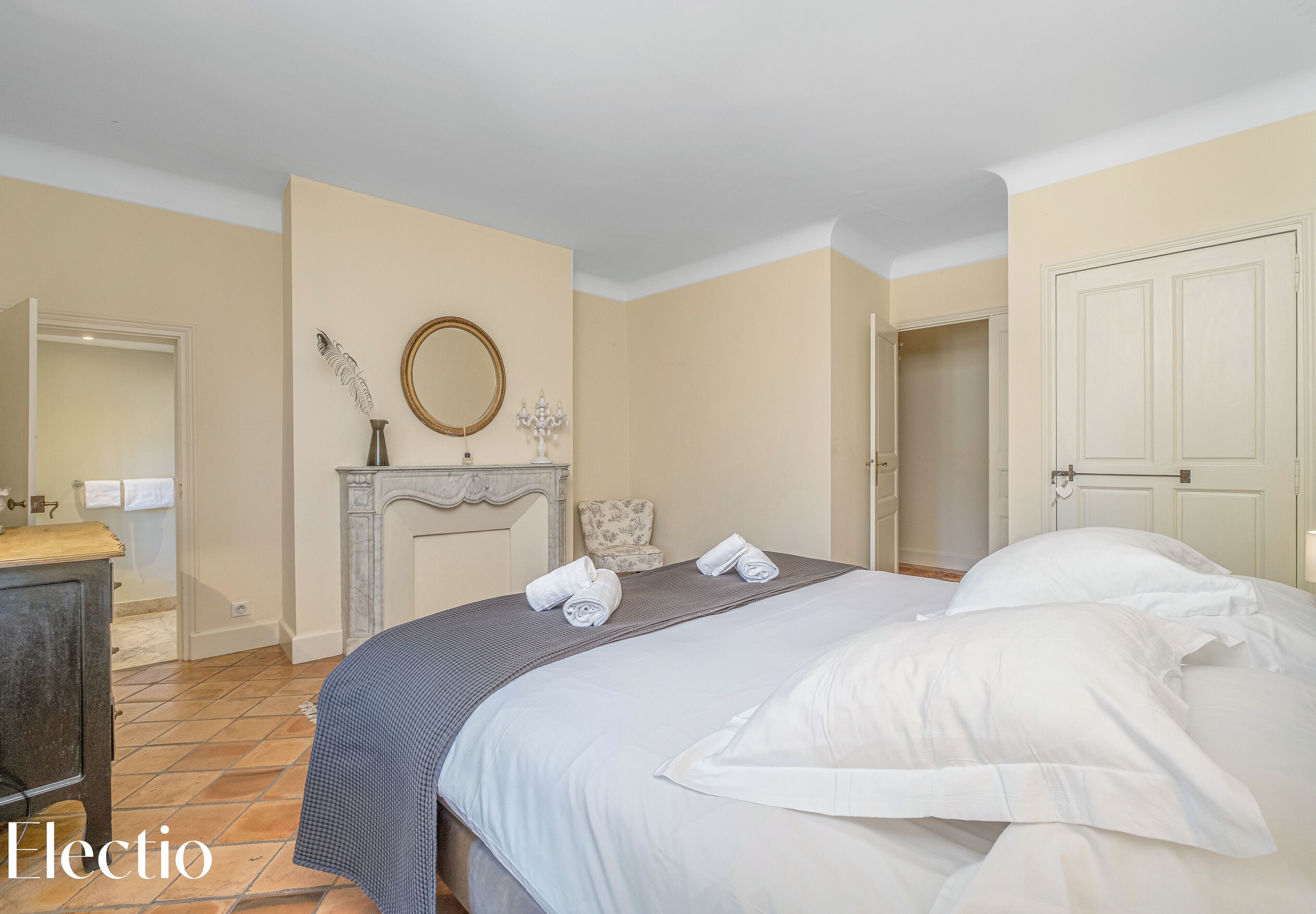 Een slaapkamer met een bed, een dressoir, een spiegel en een open haard.