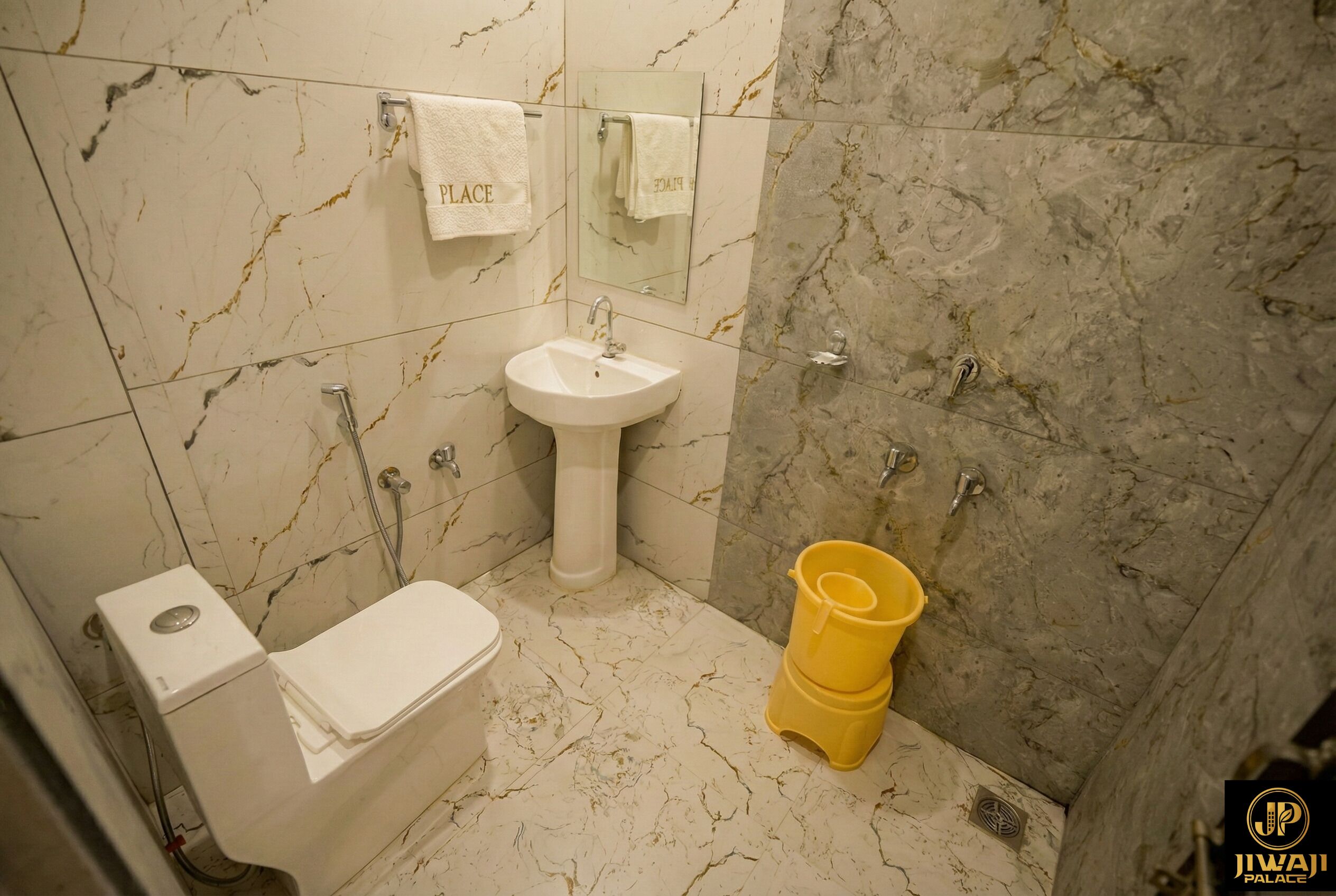 A bathroom with a marble floor, a white sink, a toilet, and a yellow bucket.
