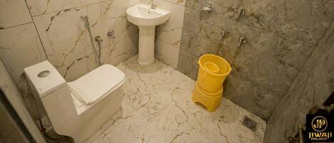 A bathroom with a marble floor, a white sink, a toilet, and a yellow bucket.