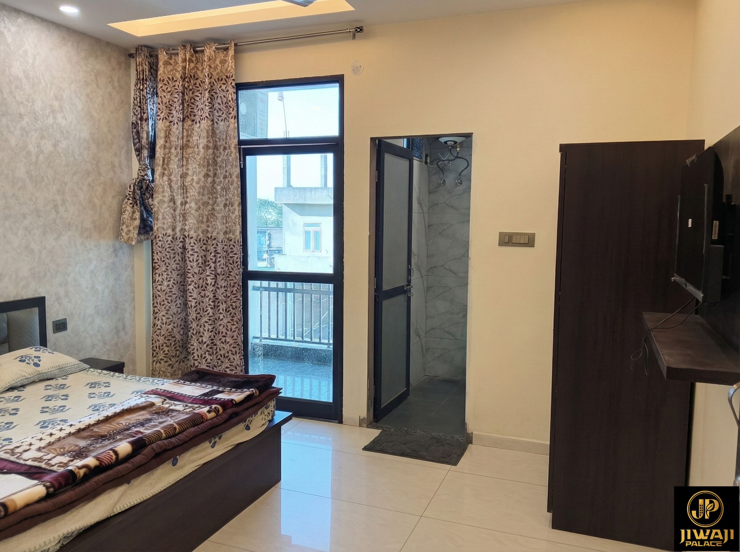 A bedroom with a bed, a wardrobe, a bathroom with a glass door, and a view of the outside.