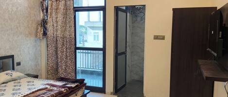 A bedroom with a bed, a wardrobe, a bathroom with a glass door, and a view of the outside.