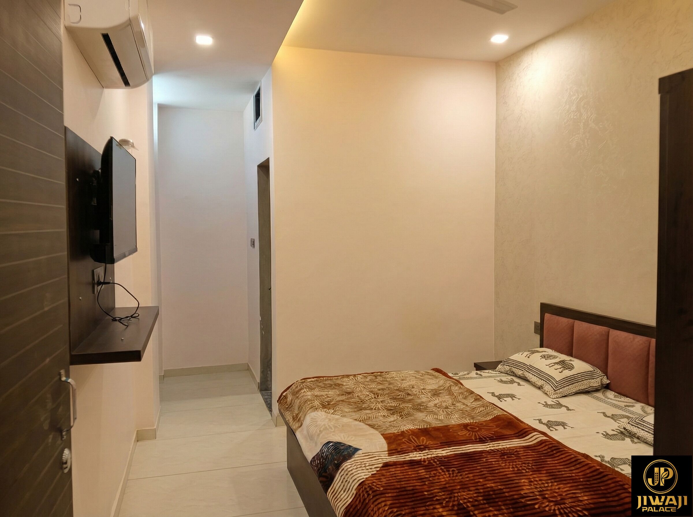 A hotel room with a bed, a television mounted on the wall, and a small window.