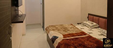 A hotel room with a bed, a television mounted on the wall, and a small window.