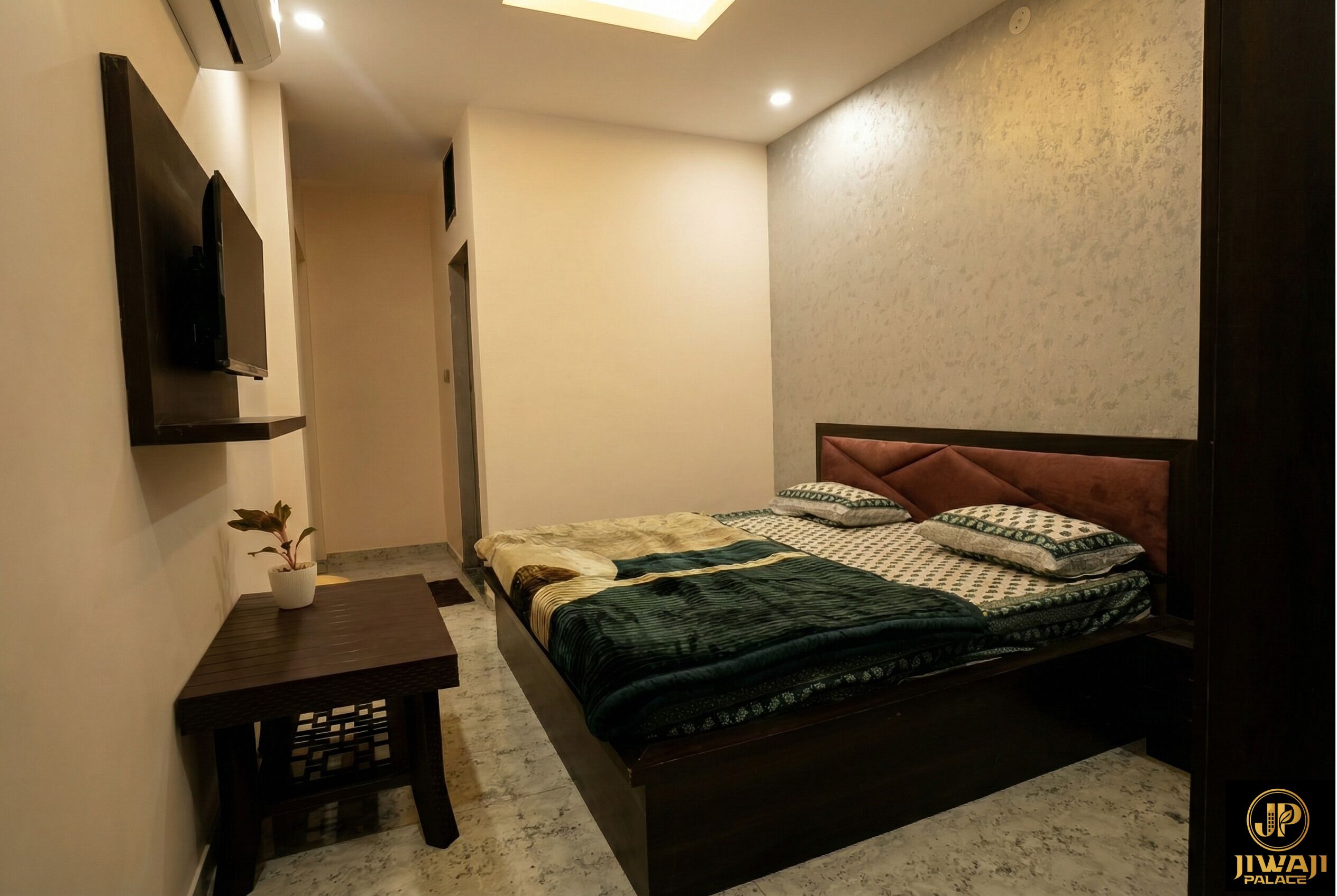 A bedroom with a bed, bedside tables, a potted plant, and a wall-mounted TV.