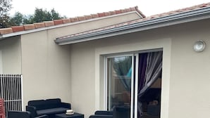 Un espacio exterior cubierto con un conjunto de sofá y una mesa, una puerta corrediza de vidrio y una reja de metal.