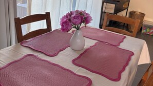 Una mesa de comedor con manteles individuales rosa, un florero con flores y sillas.