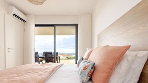 Quarto com uma cama grande, vista para o exterior e uma área de refeições visível pela porta.
