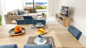 Uma sala de estar moderna com uma mesa de jantar de madeira, cadeiras estofadas azuis, um sofá e uma televisão.
