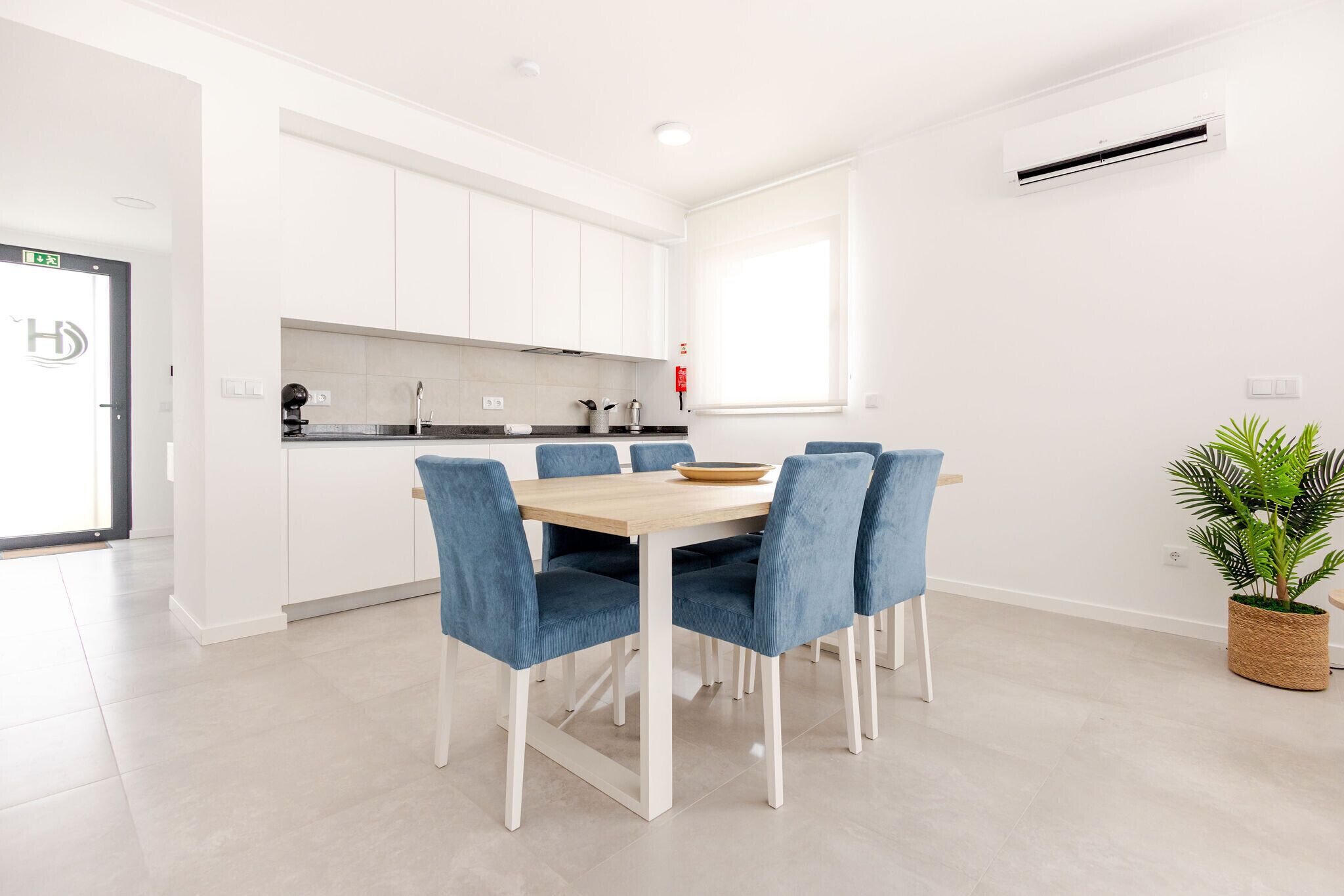 A modern kitchen with white cabinets, a wooden dining table, and blue chairs.