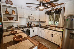 A modern kitchen with white cabinets, a stainless steel refrigerator, and a ceiling fan. - Private 3-bedroom house a three minute walk to Luna Beach (Roatan)
