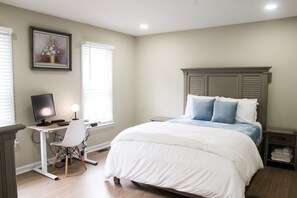 Une chambre à coucher avec un lit, un bureau avec un ordinateur, une chaise et une table de chevet.