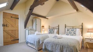 A bedroom with two beds, a wooden door, a dresser, and a nightstand with a lamp. - Beautiful Lake District Cottage With Log Burner (Penrith)