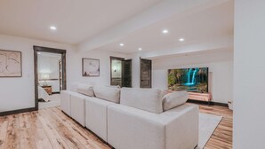 A modern living room with a sofa, a TV, and a wooden floor. - Sunrise Lookout - Lakefront | Dock | Swim | Fish (Eureka)