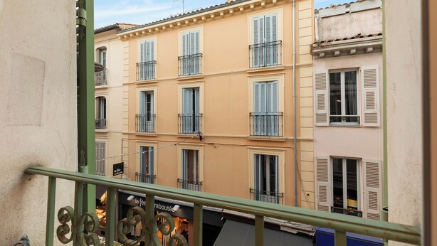 A multi-story building with balconies and shutters, viewed from a balcony with a metal railing.