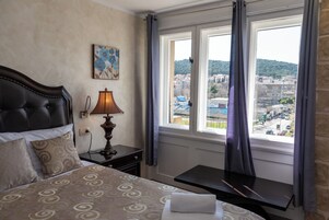 Ein Hotelzimmer mit einem Bett, einem Nachttisch mit Lampe, einem kleinen Tisch und einem Fenster mit Vorhängen.