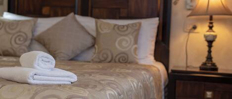 Una cama bien hecha con toallas blancas enrolladas, una colcha estampada y un cabecero de madera.