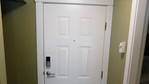 Una puerta blanca con cerradura electrónica, un felpudo negro y un interruptor de luz en la pared.