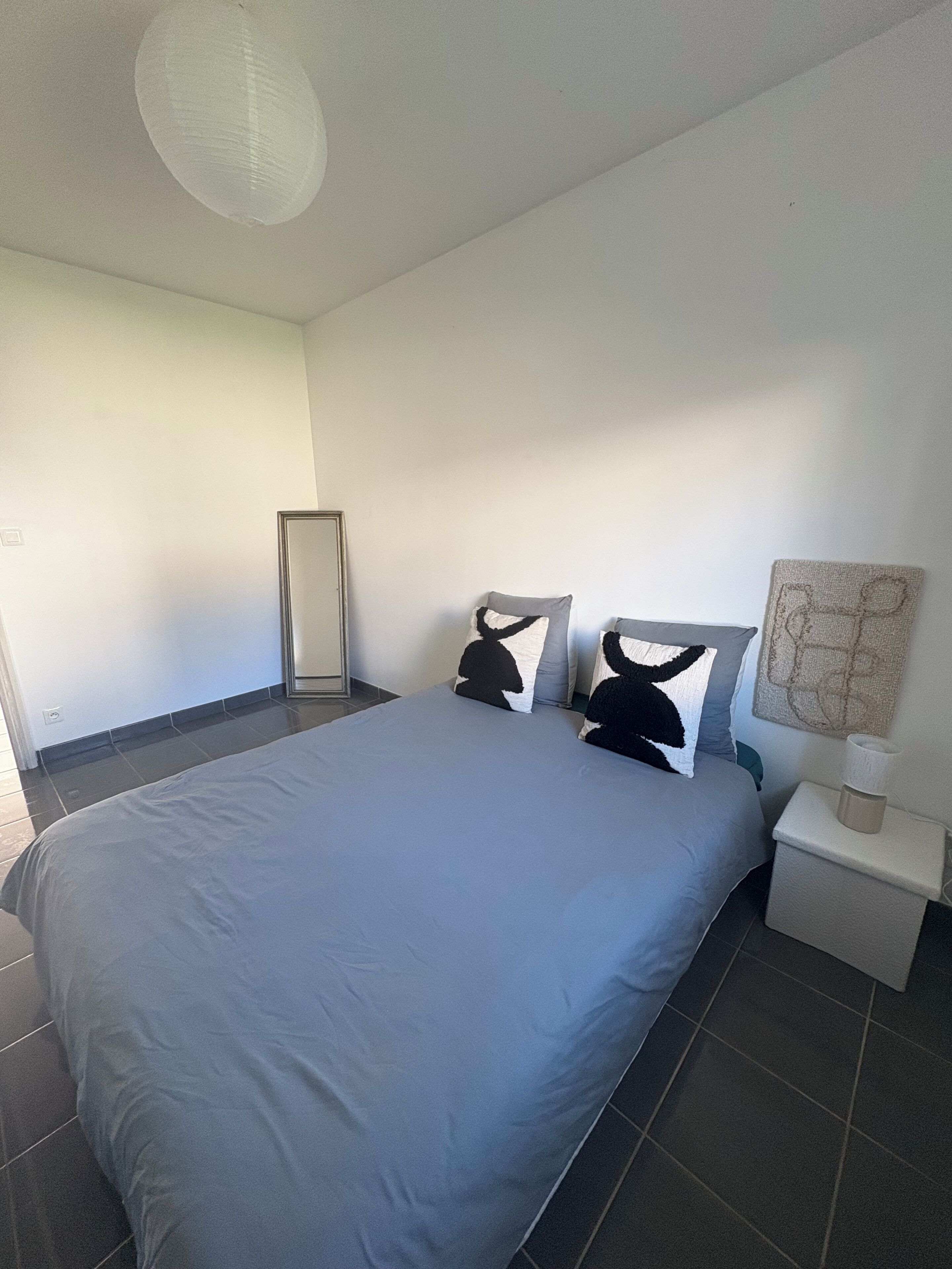 Un dormitorio con una cama grande, una mesita de noche con lámpara y una obra de arte colgada en la pared.